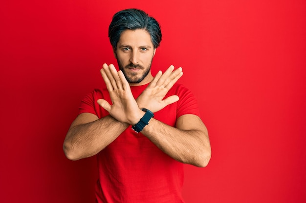 Photo gratuite jeune homme hispanique portant un t-shirt rouge décontracté expression de rejet croisant les bras faisant un signe négatif visage en colère