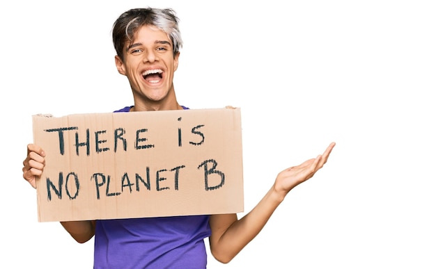 Photo gratuite jeune homme hispanique tenant il n'y a pas de bannière de planète b célébrant la victoire avec un sourire heureux et une expression de gagnant avec les mains levées