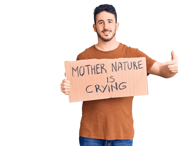 Photo gratuite jeune homme hispanique tenant mère nature pleure bannière en carton de protestation souriant heureux pointant avec la main et le doigt