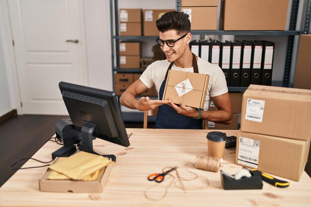 Jeune homme hispanique travailleur d'entreprise de commerce électronique ayant un appel vidéo montrant le paquet au bureau