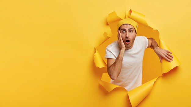 Un jeune homme impressionné touche la joue, a des expressions faciales stupéfiées