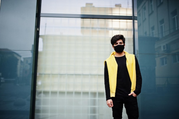 Jeune homme indien hipster urbain dans un sweat-shirt jaune à la mode Un gars sud-asiatique cool porte un sweat à capuche et un masque de protection du visage noir pendant la nouvelle normalité