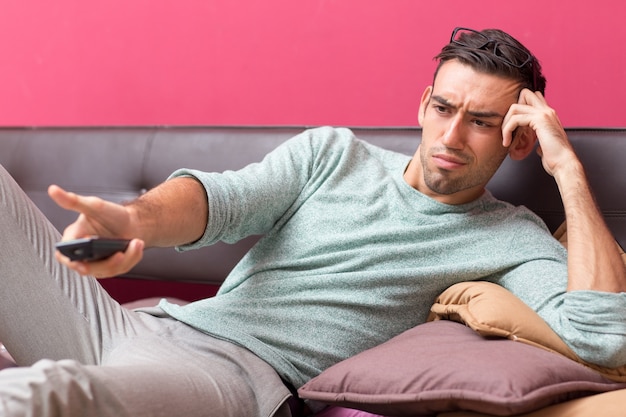 Jeune homme insatisfait change de chaîne de télévision à la maison