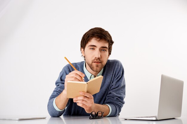 Jeune homme intelligent et réfléchi, beau, écrivant des conseils et des pensées utiles, tenez un crayon et un cahier, regardez intéressé