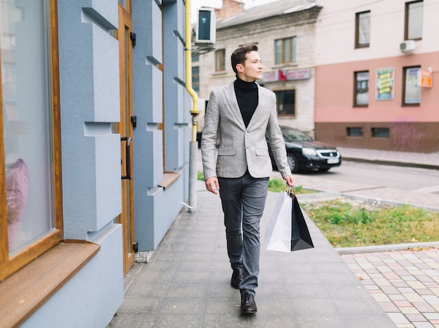 Un jeune homme intelligent, tenant des sacs de shopping, marchant dans la rue