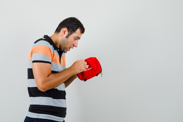 Jeune homme à l'intérieur de la trousse de premiers soins en t-shirt et à la recherche intéressée.