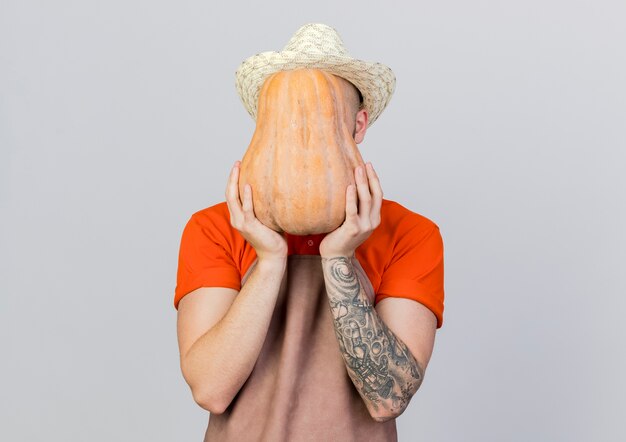 Jeune homme jardinier portant chapeau de jardinage tient la citrouille devant le visage