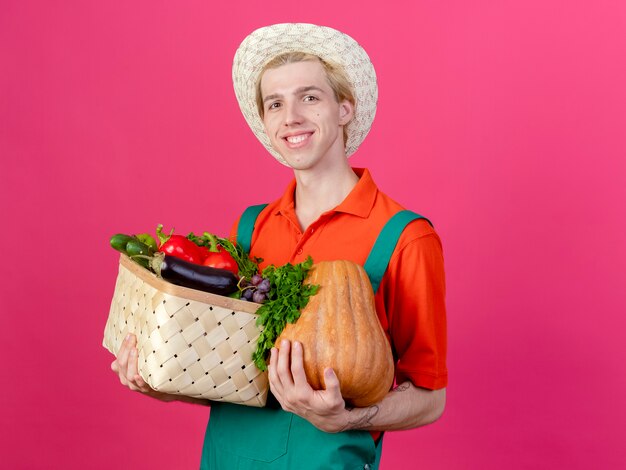 Jeune homme de jardinier portant une combinaison et un chapeau tenant une caisse pleine de légumes