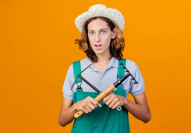 Jeune homme de jardinier portant une combinaison et un chapeau tenant un mini râteau