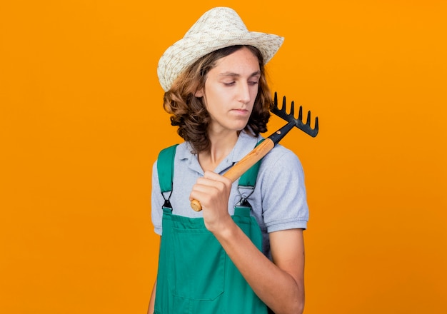Photo gratuite jeune homme de jardinier portant une combinaison et un chapeau tenant un mini râteau