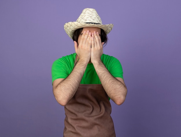 Jeune homme jardinier en uniforme portant chapeau de jardinage visage couvert avec les mains