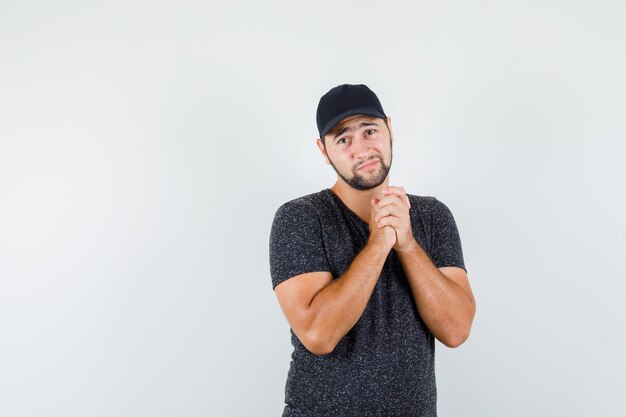 Jeune homme joignant les mains en geste de prière en t-shirt et casquette et à la recherche d'espoir