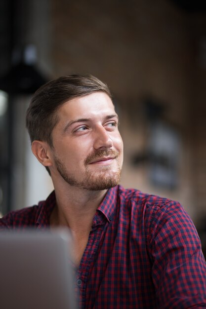 Jeune homme joli pensif qui travaille sur un ordinateur portable