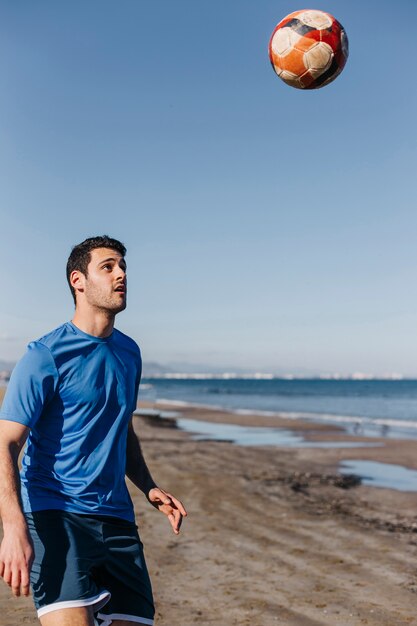 Jeune homme jouant au football à la plage