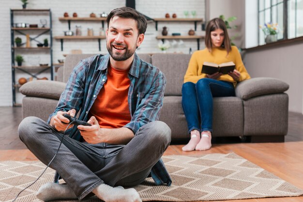 Jeune homme jouant au jeu vidéo avec joystick et sa femme assise sur un canapé en toile de fond