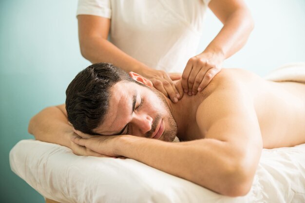 Jeune homme latin très détendu recevant un massage des tissus profonds sur le dos dans une clinique de bien-être et de spa