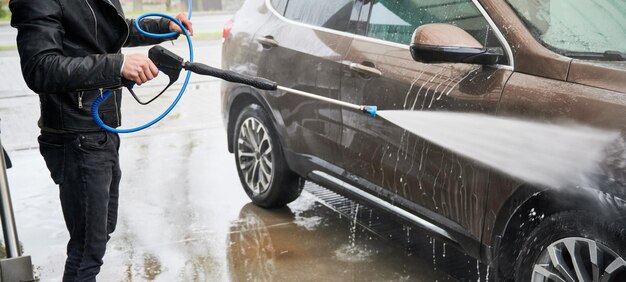 Jeune homme laver la voiture sur la station de lavage de voiture en plein air