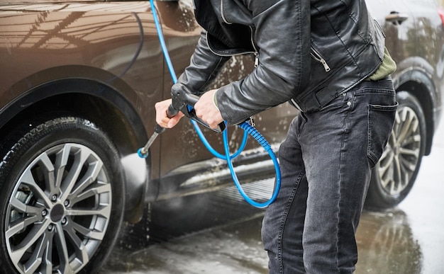 Jeune homme laver la voiture sur la station de lavage de voiture en plein air