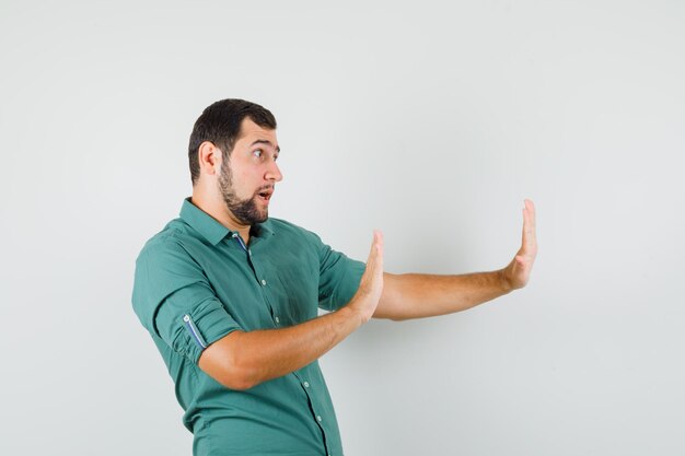 Jeune homme levant les bras pour rejeter quelque chose en chemise verte et semblant concentré, vue de face.