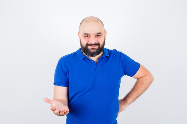 Jeune homme levant la main avec la paume ouverte tout en souriant en chemise bleue et l'air heureux, vue de face.