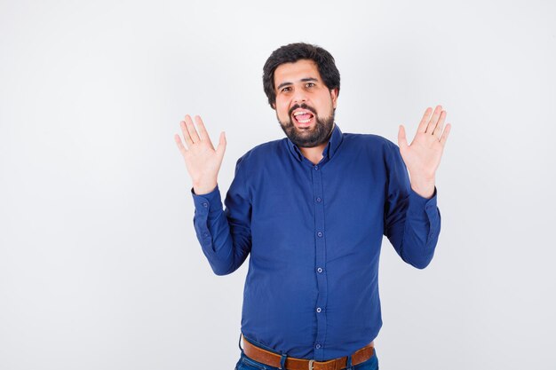 Jeune homme levant la main pour avoir refusé quelque chose en chemise bleu royal, vue de face.