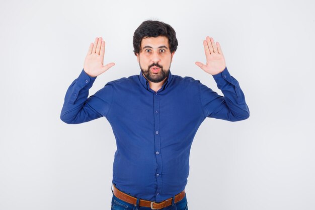 Jeune homme levant la main pour se rendre en vue de face de la chemise bleu royal.