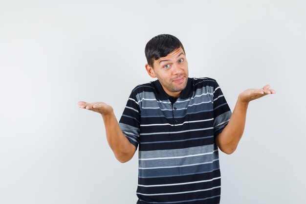 Jeune homme levant les mains comme tenant ou montrant quelque chose en t-shirt et regardant gai, vue de face.