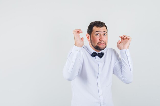 Jeune homme levant les mains dans un geste impuissant en chemise blanche et à la peur, vue de face.