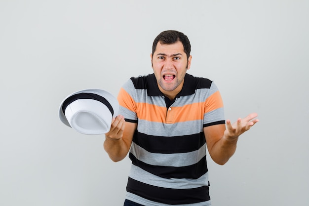 Photo gratuite jeune homme levant les mains avec une manière agressive en t-shirt et à la nervosité. vue de face.