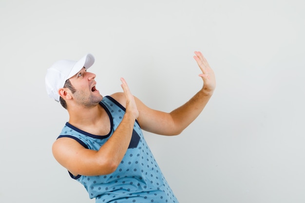 Jeune homme levant les mains pour se défendre en maillot bleu, casquette et à la peur. vue de face.