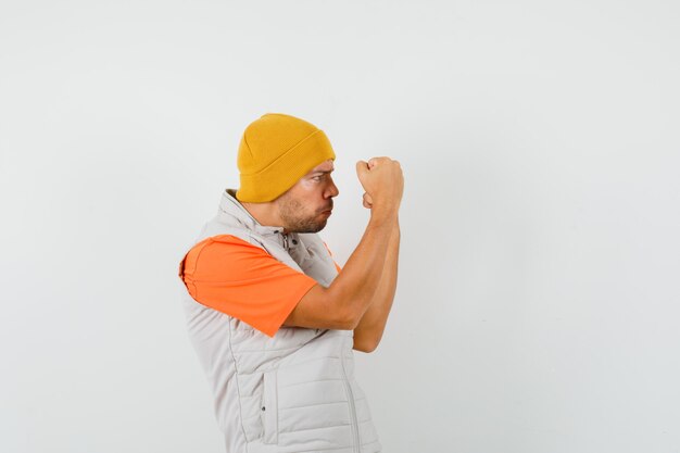 Jeune homme levant les poings serrés en t-shirt, veste, chapeau et à forte