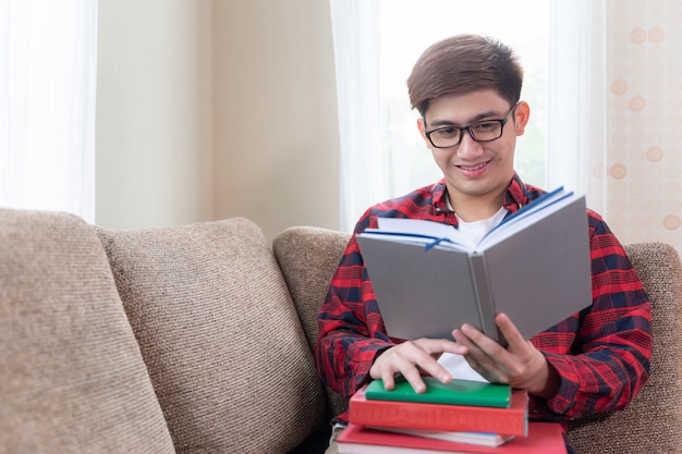 Jeune homme lisant un livre avec joyeuse sur un canapé à la maison