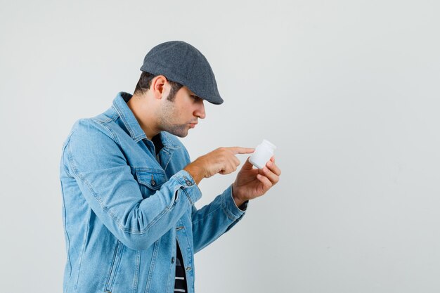 Jeune homme lisant le nom de pilules en veste, casquette et à la recherche concentrée. .