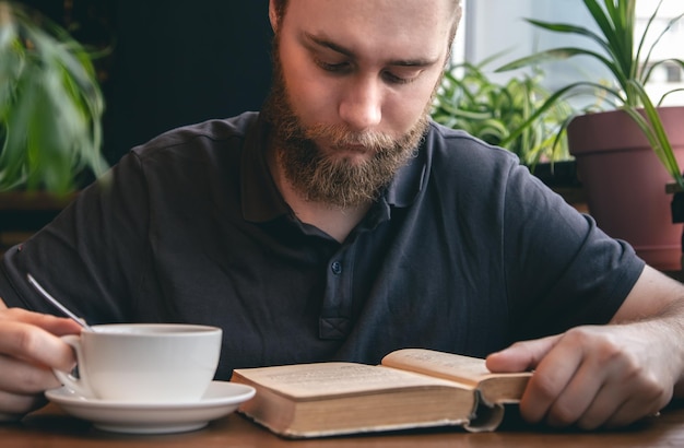 Photo gratuite un jeune homme lit un livre autour d'une tasse de thé dans un café
