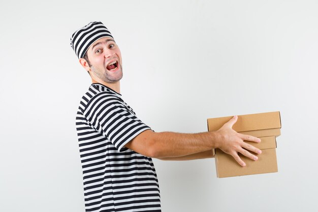 Jeune homme livrant des boîtes en carton en t-shirt, chapeau et à la joyeuse. .