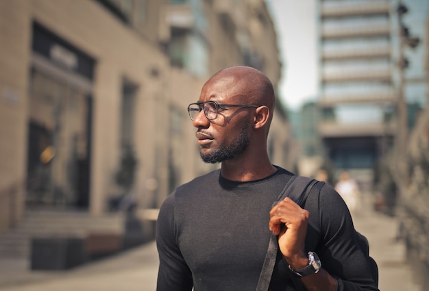 Photo gratuite jeune homme avec des lunettes portant un t-shirt noir et un sac à dos dans la rue