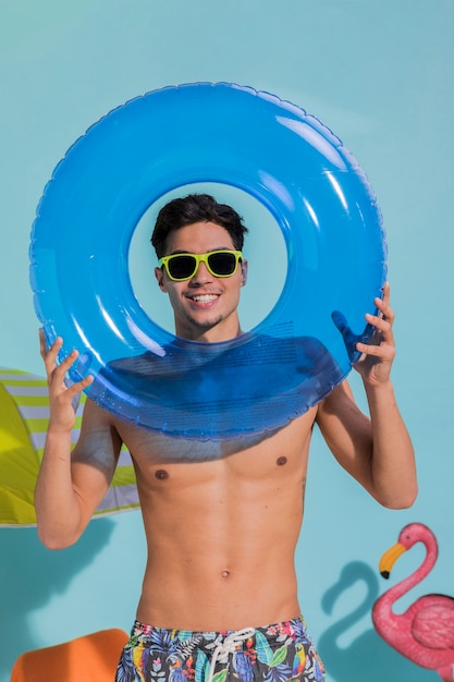 Jeune homme à lunettes de soleil tenant une bouée de sauvetage bleue