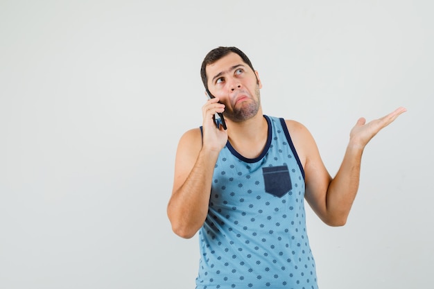 Jeune homme en maillot bleu parlant au téléphone mobile et à la confusion