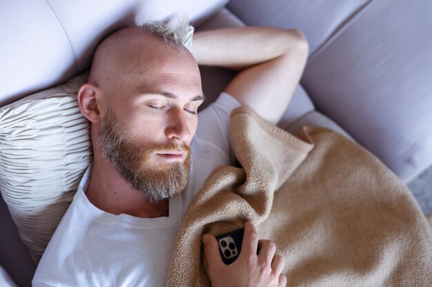 Un jeune homme à la maison s'est endormi sur le canapé avec un téléphone portable