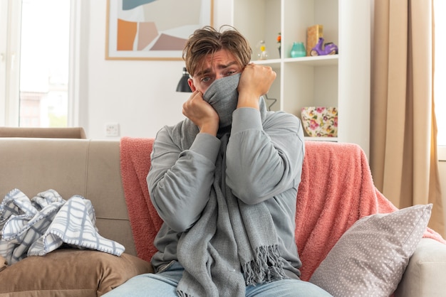 jeune homme malade couvrant sa bouche avec un foulard assis sur un canapé dans le salon