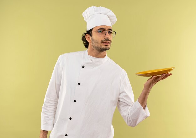 Un jeune homme malheureux cuisinier portant l'uniforme de chef et des verres tenant la plaque