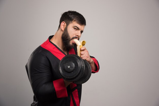 Jeune homme mangeant une banane et tenant un haltère.