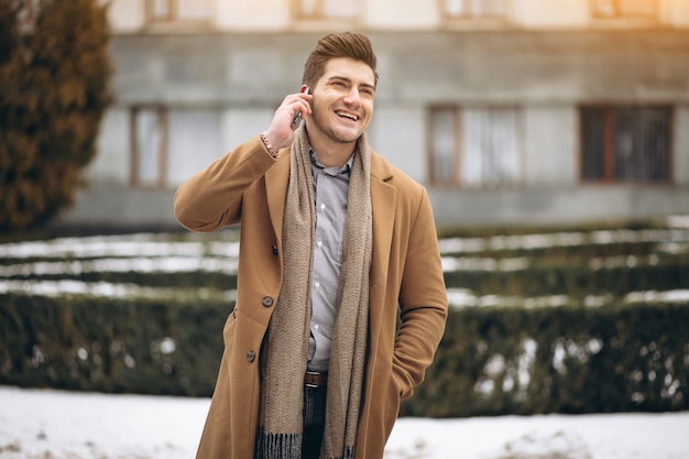 Jeune homme en manteau parler au téléphone à l&#39;extérieur