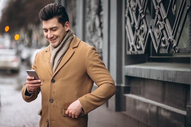 Jeune homme en manteau parler au téléphone à l&#39;extérieur