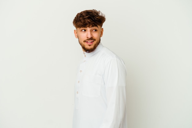 Jeune homme marocain vêtu d'un vêtement arabe typique isolé sur un mur blanc regarde de côté souriant, gai et agréable.