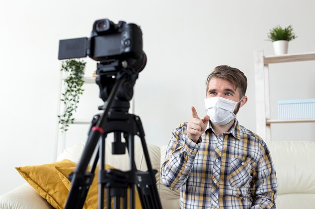 Jeune homme avec masque facial enregistrement vidéo à la maison