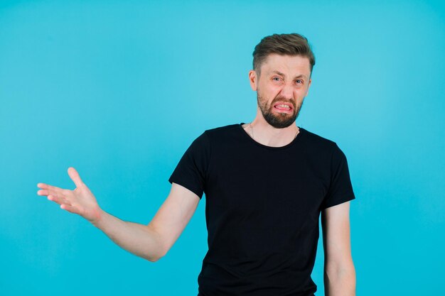 Un jeune homme mécontent lève la main vers la gauche sur fond bleu