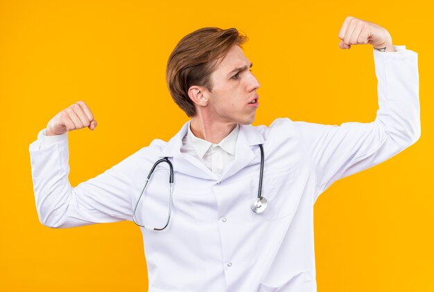 Jeune homme médecin confiant portant une robe médicale avec un stéthoscope montrant un geste fort