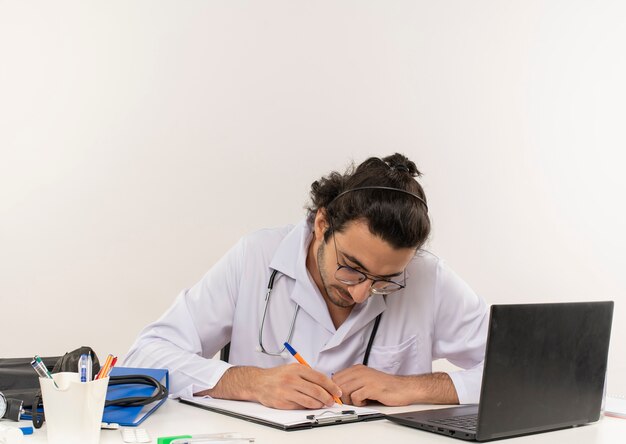 Jeune homme médecin avec des lunettes médicales portant une robe médicale avec stéthoscope assis