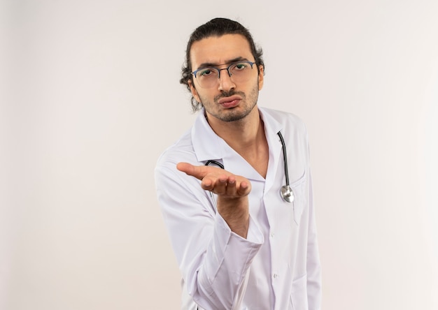 Jeune homme médecin avec des lunettes optiques portant une robe blanche avec stéthoscope montrant le geste de baiser